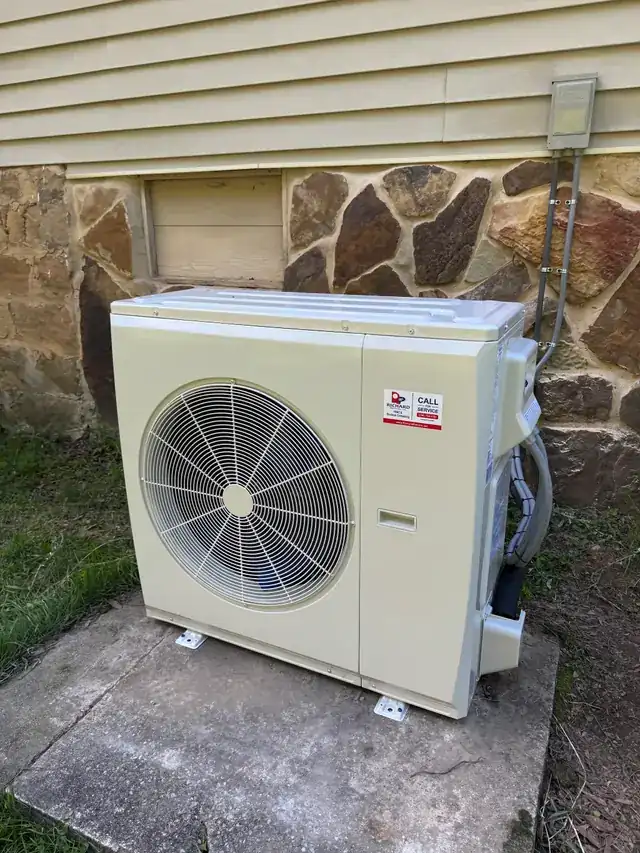 A ductless mini-split condenser mounted beside a stone-faced home