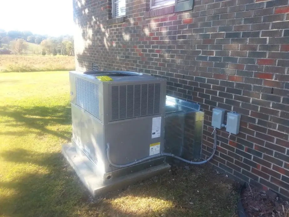 A new packaged air conditioning unit on its pad beside a brick wall with hills behind