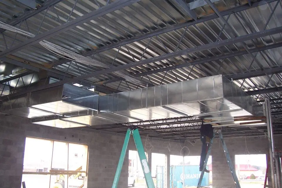 Galvanized ductwork hung from steel trusses with a Richard Electric technician on a ladder